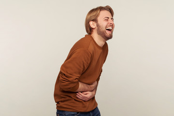 Hilarious laughter. Portrait of amused man with beard wearing sweatshirt holding belly and laughing...