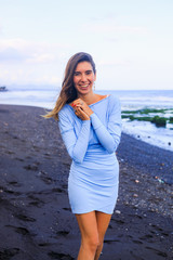 Beautiful young woman walking on black sand beach. Caucasian woman wearing blue mini dress. Romantic concept. Travel lifestyle.