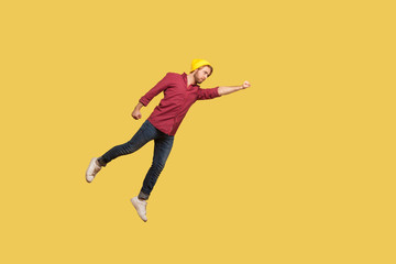 Fototapeta na wymiar Determined serious ambitious guy flying in air with raised hand, striving forward to victories, feeling super hero power, freedom and confidence to achieve goal. indoor studio shot, yellow background