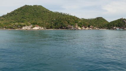 Calm water near green tropical exotic paradise island. Tranquil sea water near diving resort on hilly green Tao Island on cloudy day in Thailand. View from the boat.