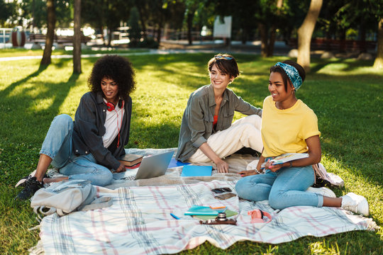 Image of multinational women doing homework with laptop in summer park