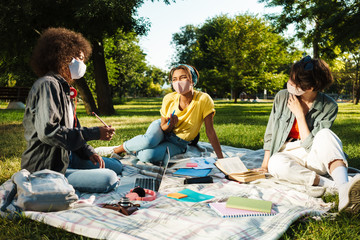 Image of multinational women doing homework with laptop in summer park