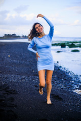 Fototapeta na wymiar Beautiful young woman walking on black sand beach. Caucasian woman wearing blue mini dress. Romantic concept. Travel lifestyle.