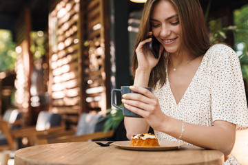 Image of young woman smiling and talking on cellphone in cafe outdoors