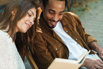 Image of happy multinational couple smiling and reading book