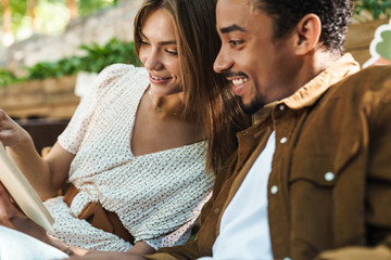 Image of happy multinational couple smiling and reading book