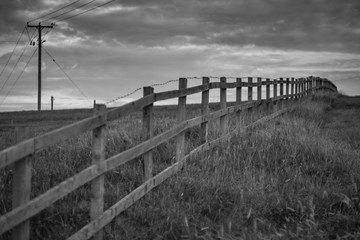Black and white image of a wooden fence in a field receding into the distance