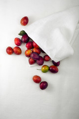 Ripe colorful plums with green leaves on a white table.