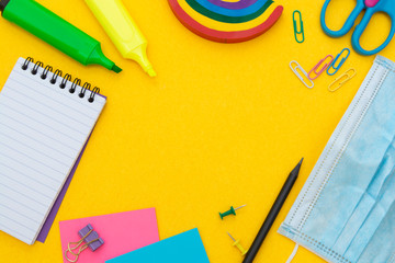Back to school concept. Face mask, colorful pencils, rainbow eraser, notebook, sticky notes and office supplies. Flat lay. Abstract educational background.