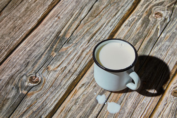 Milk in an enameled light blue mug on a rough wooden table