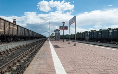 View of the railway tracks from the station platform. Cars standing on the tracks. Freight car. Railway station with a platform. Traveling by rail.
