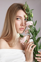 Beauty portrait  woman with pink eustoma flowers in her hands. Natural cosmetics for face and body skin care. Beautiful girl in a white shirt