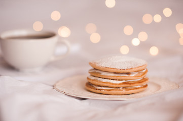 Stack of tasty pancakes with cream over cup of tea nad glowing lights at background. Selective focus. Good morning.