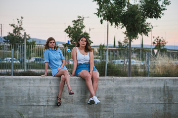 Two young women sitting in a city. They are meeting on a summer afternoon.