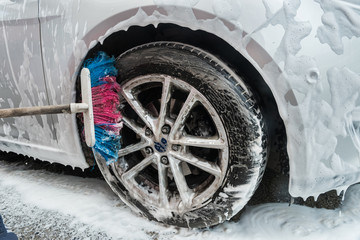 female hand cleaning car in service with tools soap foam and water.