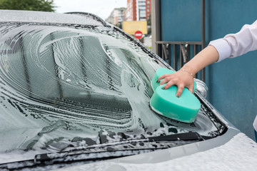 hand hold  sponge with white foam over the car for washing