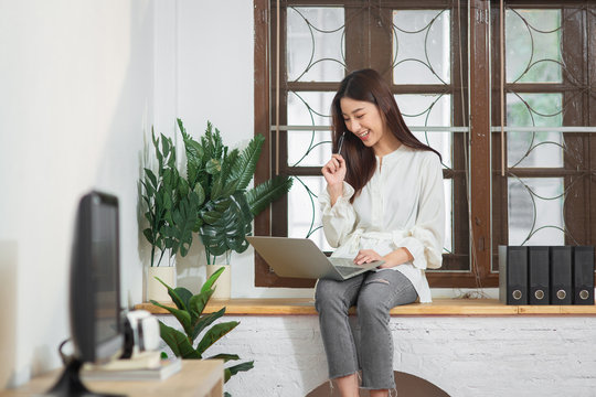Young Entrepreneur Asian business woman working at home office with internet using laptop, Happy female look at computer screen listen and learning online courses at apartment