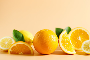 Whole and cut oranges and lemons with green leaves on orange color background