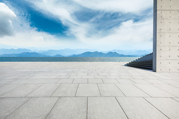 Empty square floor and lake with mountains under blue sky.