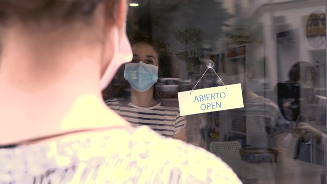 Clerk woman owner of a commercial shop wearing a face mask opening her business to a client. New normality lifestyle.