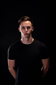 Portrait of a young athletic man in a black T-shirt on a black background. Young beautiful sporty man.