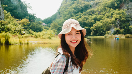 Cheerful young traveler Asian lady with backpack walking at the mountain lake. Korean teen girl enjoy her holidays adventure feeling happy freedom. Lifestyle travel and relax in free time concept.