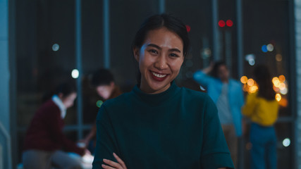 Portrait of successful executive businesswoman smart casual wear looking at camera and smiling, happy in modern night office workplace. Young Asia lady standing relax in contemporary meeting room.