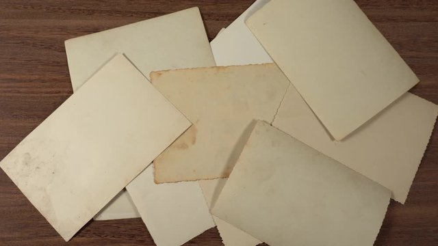 Stack of old vintage paper photos appear stacked together on brown wooden table surface background. Back view of photo pictures.
