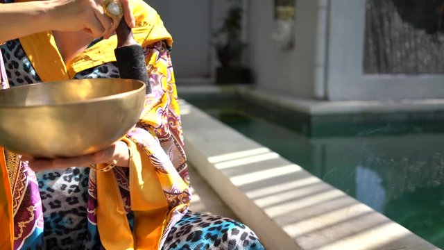 attractive young pregnant woman in colored atlas kimono dress with a singing bowl sitting and playing on summer terrace 