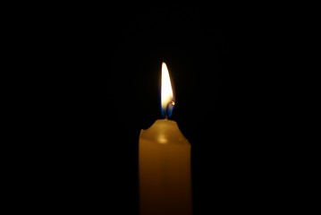Burning candle on a black background in the dark at night.