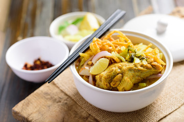 Northern Thai food (Khao Soi), Spicy curry noodles soup with chicken in a bowl eating with crispy deep-fried egg noodles, pickled mustard, shallots, lime and ground chillies fried in oil