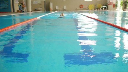 young sportswoman in swimsuit and goggles swims butterfly stroke style in pool clear water at modern gym at bright light slow motion