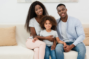 african american family looking at camera and sitting on sofa in living room