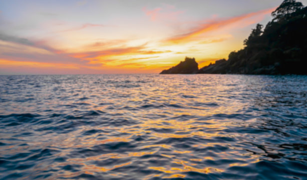 Blur background of indigo blue ocean in the evening, the sun was setting, reflections fell on the wave surface with golden warm light. The sky is clear and clean. Feeling refreshed and relaxed.