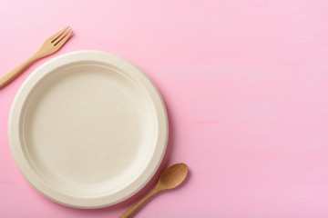 Biodegradable plate, Compostable plate or Eco friendly disposable plate with wooden fork and spoon on pink background