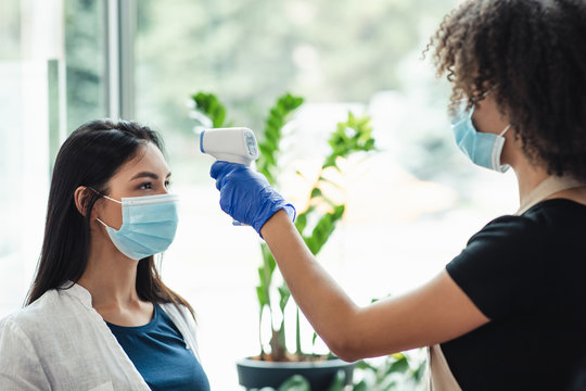 Woman checking temperature to client using infrared tool in beauty salon