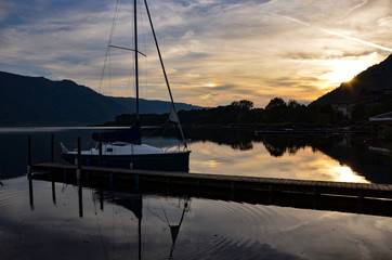 Sunset at Ossiacher lake in Kaernten (Carinthia) in Austria, sailboat at the dock, reflections of sunlight on water surface, autumn 