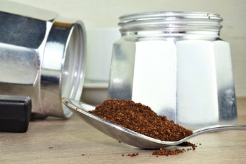 Coffee in a spoon on a wooden table, coffee maker and white cup in the background