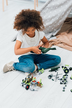 curly african american kid playing with plastic toys and sitting on floor