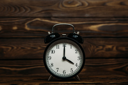 Clock on a wooden background. The clock shows the time of four o'clock in the afternoon. The clock shows the time four o'clock in the morning. An image of a retro clock showing 04:00 pm/am. Copy space