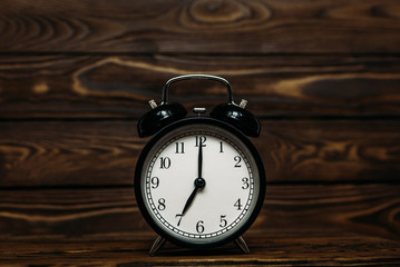Clock on a wooden background. The clock shows the time of seven o'clock in the afternoon. The clock shows the time seven o'clock in the morning. An image of a retro clock showing 07:00 pm/am. 