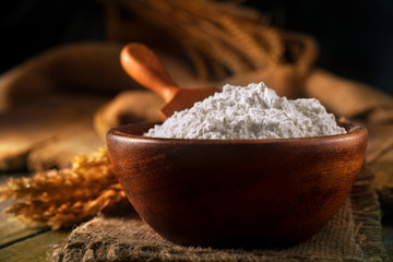 Flour in a bowl with a flour spoon, on a rustic wooden background. Close up, side view, high-resolution product image.