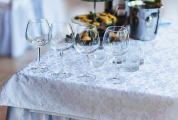 Empty glass goblets, champagne glasses, wines are in a row on a table with a white tablecloth in a restaurant for guests and parties. Dishes for a buffet, banquet.
