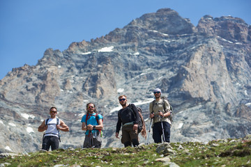 Fototapeta premium From below view of group of four tourists posing with trekking equipment, looking at camera, beautiful mountain Matterhorn with snow on background. Mountain hiking, alpinism. Sport tourism in Alps.