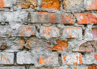The texture of an old, destroyed wall and a building made of red, orange uneven bricks with cracks, gray cement and concrete. Photography, abstraction, background.