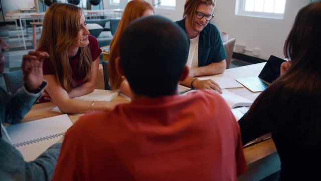 College classmates smiling during group study. Cheerful male and female students sitting around a table in university for group study.
