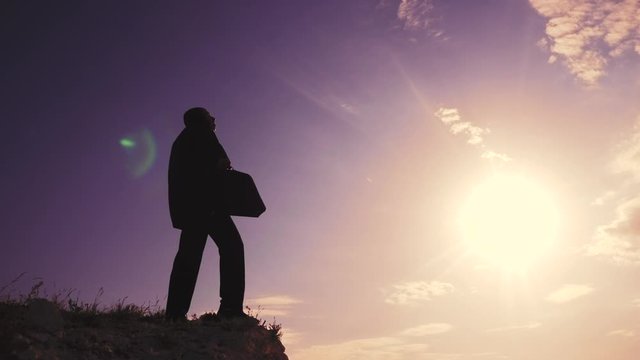 business success teamwork concept. man businessman in a jacket with a silhouette suitcase rises to the top of mountain looks into the distance, shows hand direction. manager lifestyle head set a goal