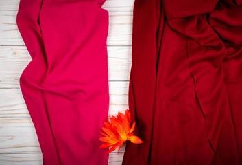 Folds of pink and red textile or fabric and artificial orange flower on white wooden board (with copyspace for text)