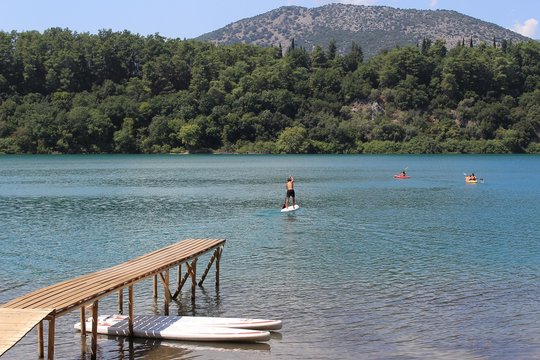 Canoeing, kayaking and sup standup paddleboarding at Ziros lake in Preveza Greece at summer holidays. Wooden pier at the foreground, green forest at the background