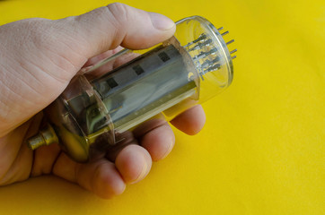 Male hand holds a vacuum tube on a yellow background.